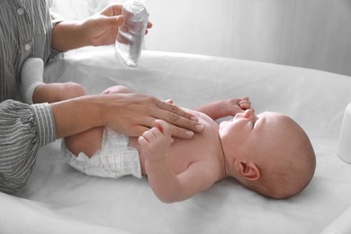 Photo of Mother massaging her baby with oil on changing table indoors, closeup