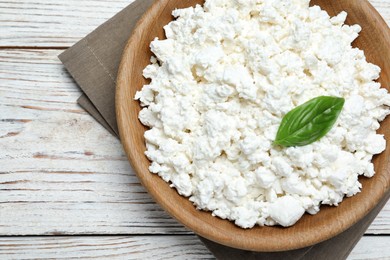 Photo of Delicious cottage cheese with basil on white wooden table, top view
