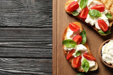 Toasted bread with tasty cream cheese and tomatoes on wooden table, flat lay. Space for text