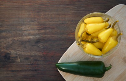 Photo of Fresh and pickled jalapeno peppers on wooden table, top view. Space for text