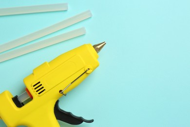 Yellow glue gun and sticks on turquoise background, flat lay. Space for text
