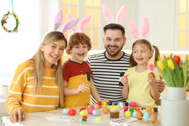 Photo of Painting Easter eggs. Happy family with bunny ears at white marble table in kitchen