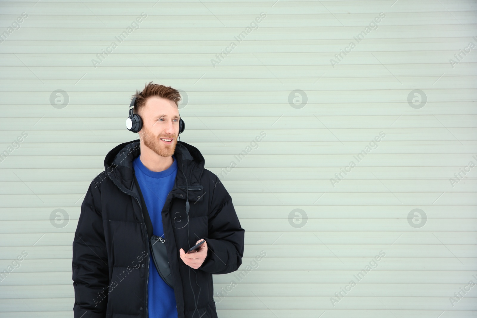 Photo of Young man listening to music with headphones against light wall. Space for text