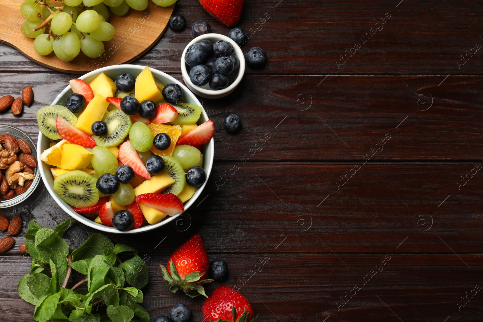 Photo of Tasty fruit salad in bowl and ingredients on wooden table, flat lay. Space for text