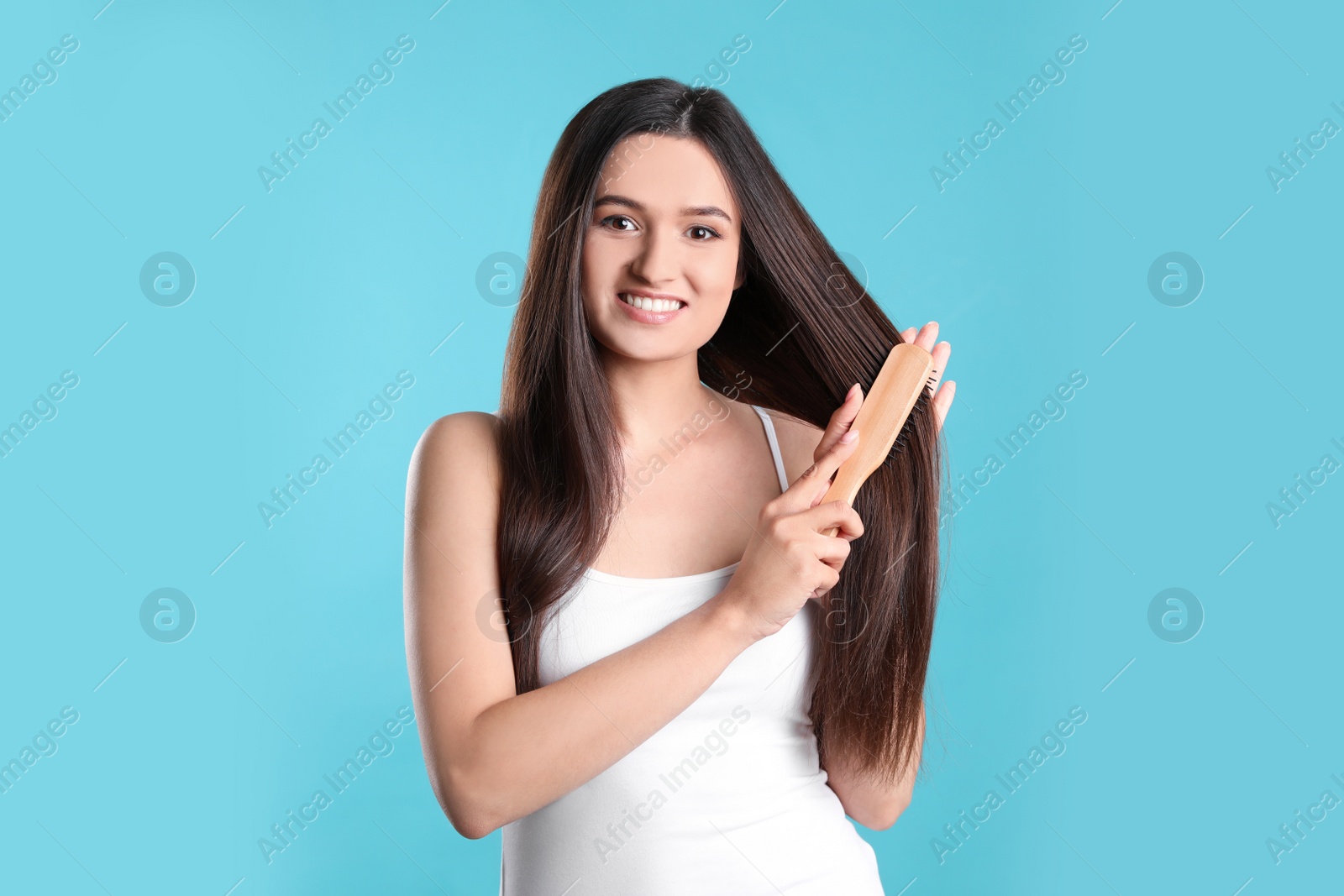 Photo of Beautiful smiling young woman with hair brush on color background