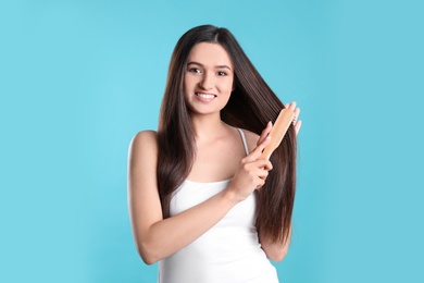 Beautiful smiling young woman with hair brush on color background