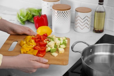 Woman holding wooden board with cut vegetables in kitchen, closeup