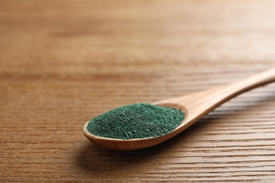 Photo of Spoon of spirulina powder on wooden background, closeup. Space for text
