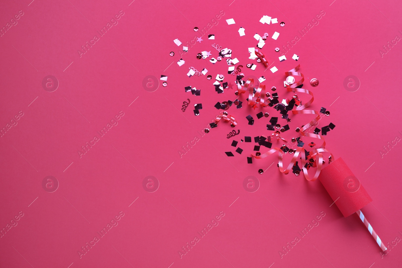 Photo of Shiny confetti and streamers with party cracker on pink background, top view. Space for text