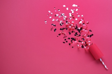 Photo of Shiny confetti and streamers with party cracker on pink background, top view. Space for text