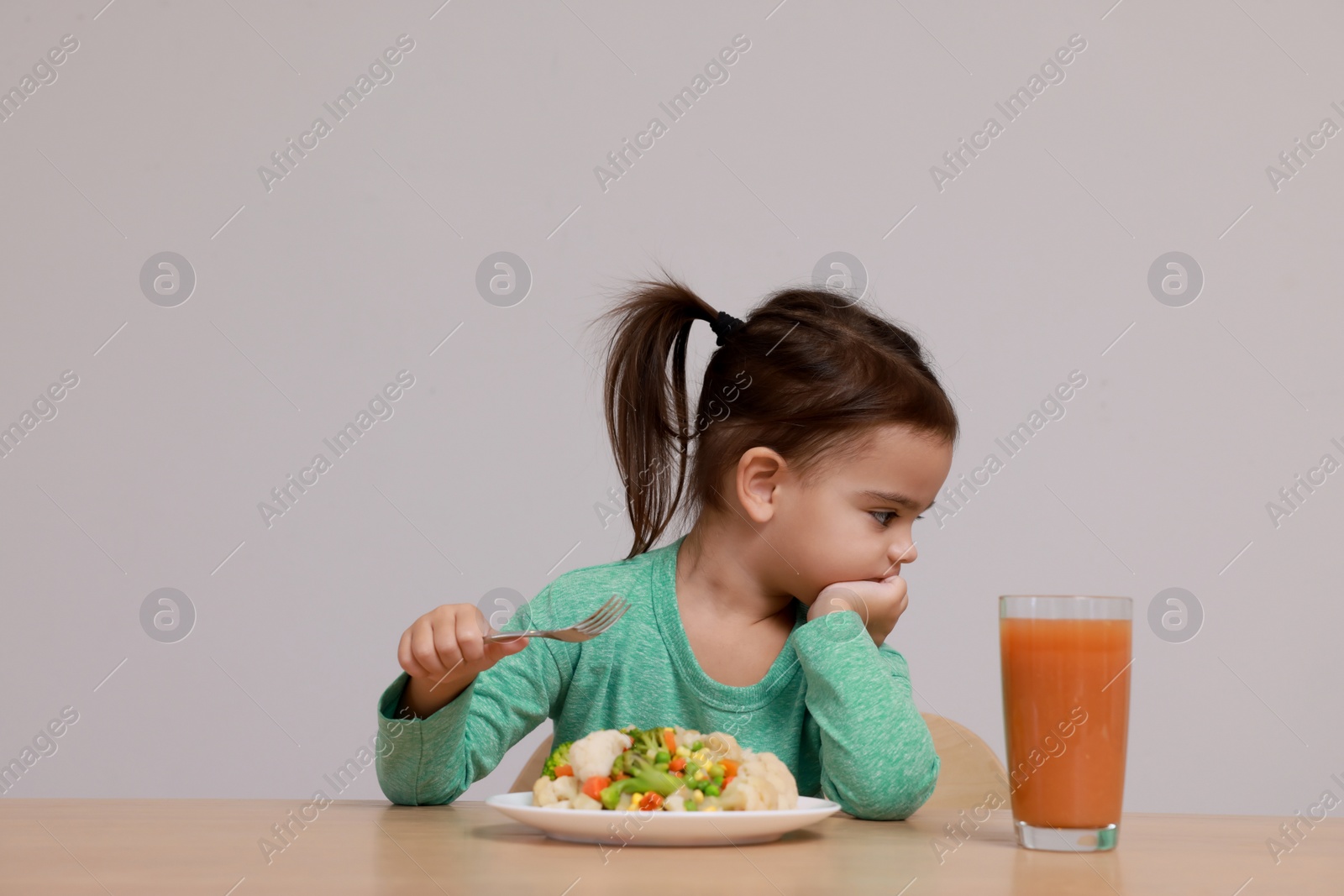 Photo of Cute little girl refusing to eat vegetable salad at table on grey background