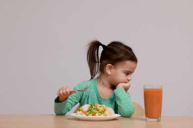Photo of Cute little girl refusing to eat vegetable salad at table on grey background