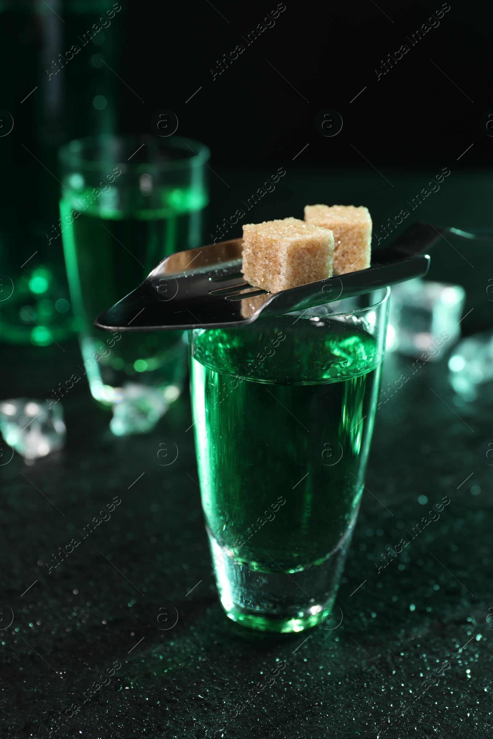 Photo of Absinthe in shot glass, spoon and brown sugar cubes on gray table, closeup. Alcoholic drink