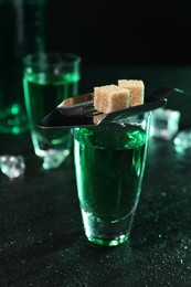 Absinthe in shot glass, spoon and brown sugar cubes on gray table, closeup. Alcoholic drink