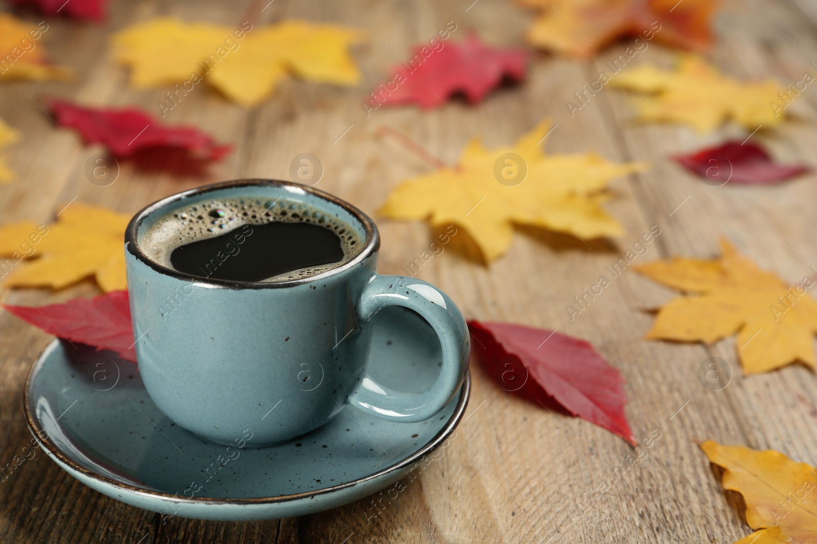 Photo of Cup of hot coffee and autumn leaves on wooden table, space for text