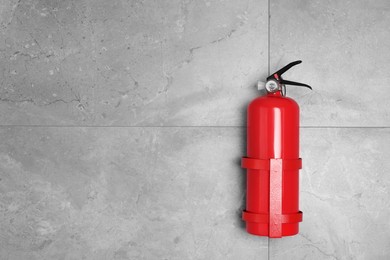 Photo of Fire extinguisher on grey wall, space for text