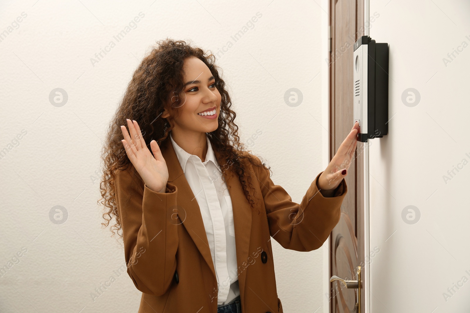 Photo of Young African-American woman ringing intercom while waving to camera in entryway