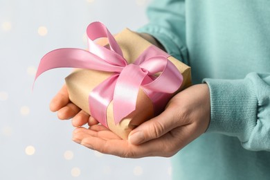 Woman holding gift box with pink bow against blurred festive lights, closeup. Bokeh effect