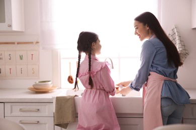 Mother and daughter washing dishes together in kitchen