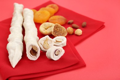 Delicious churchkhelas, nuts and dried fruits on red background, closeup. Space for text
