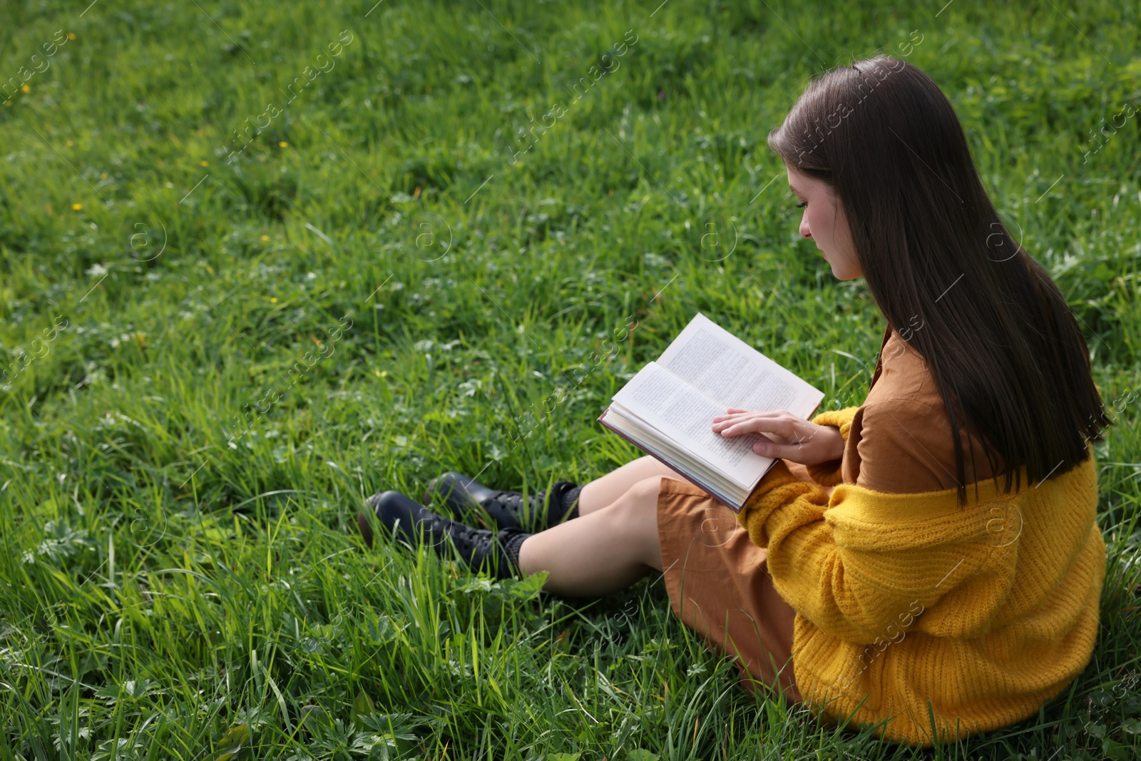 Photo of Young woman reading book on green grass