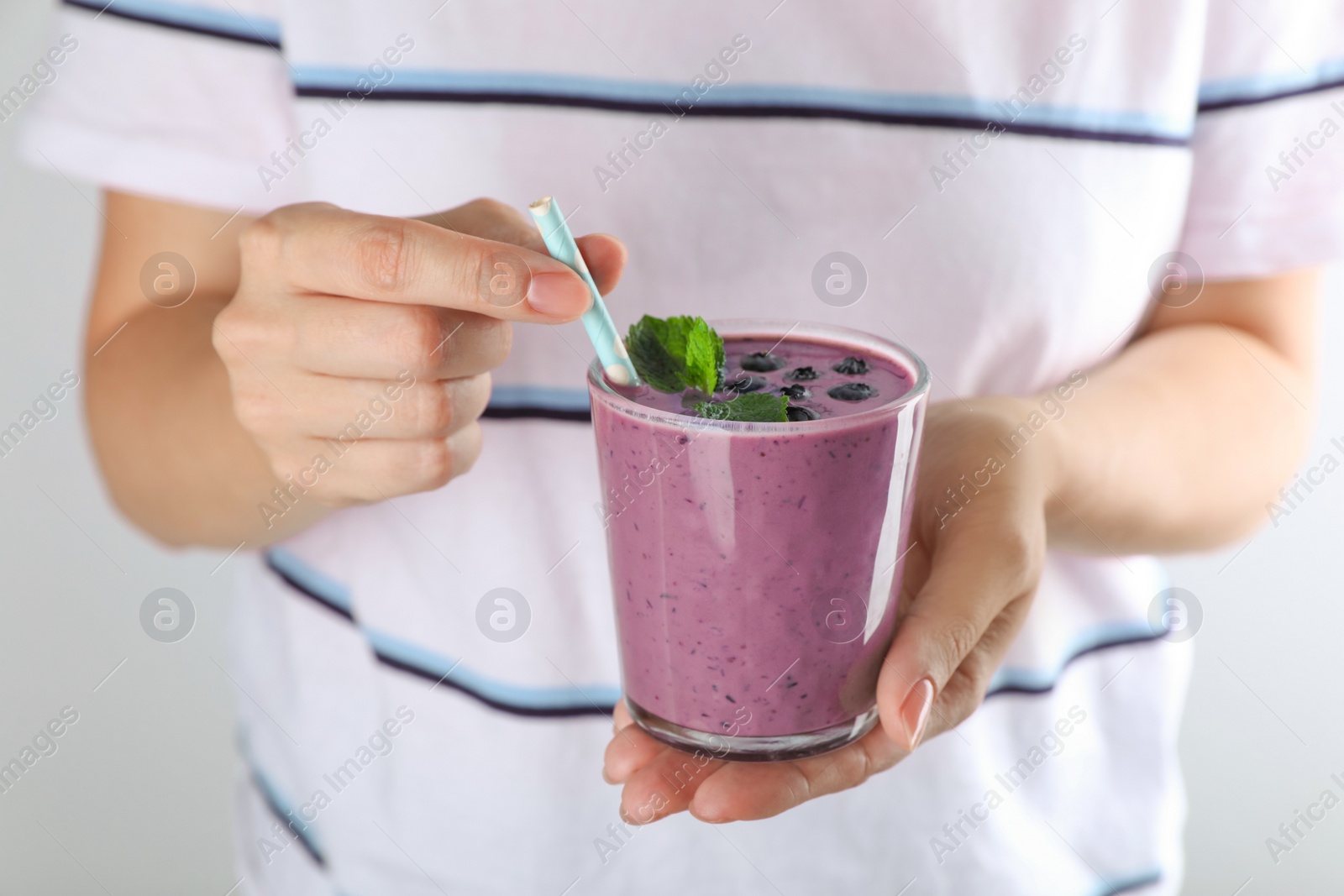 Photo of Woman with tasty blueberry smoothie against light grey background, closeup