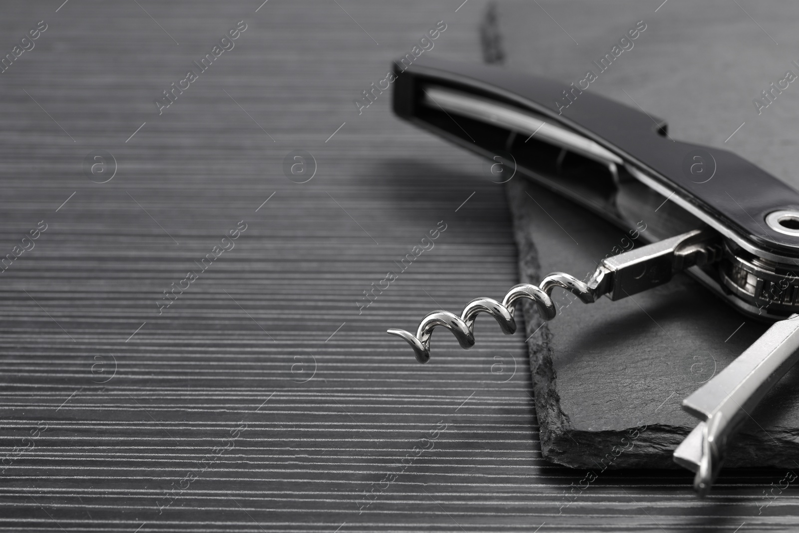 Photo of One corkscrew (sommelier knife) on black wooden table, closeup. Space for text