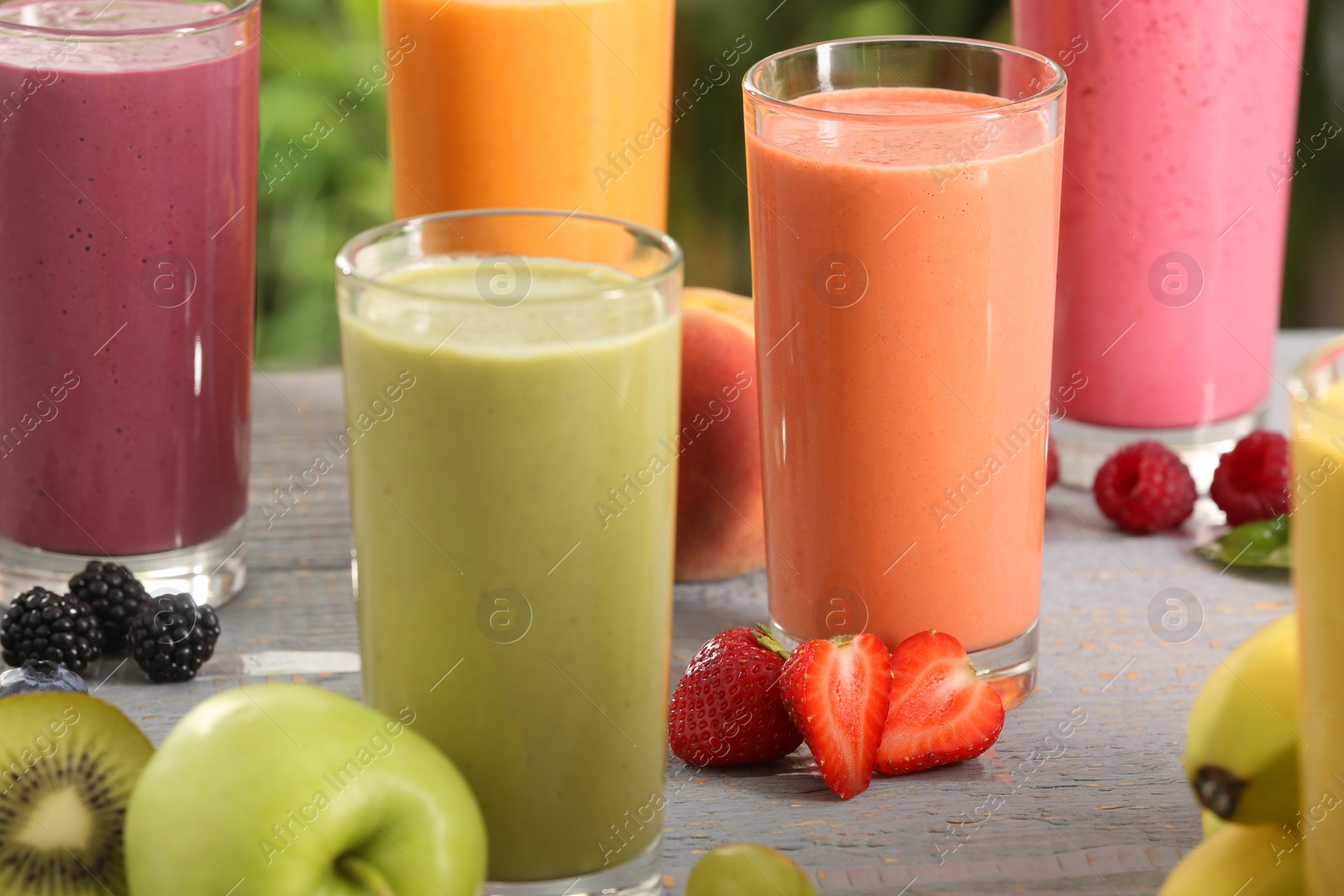 Photo of Many different delicious smoothies and ingredients on grey wooden table, closeup
