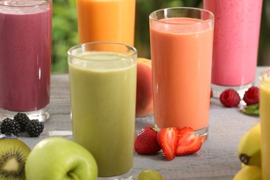 Photo of Many different delicious smoothies and ingredients on grey wooden table, closeup