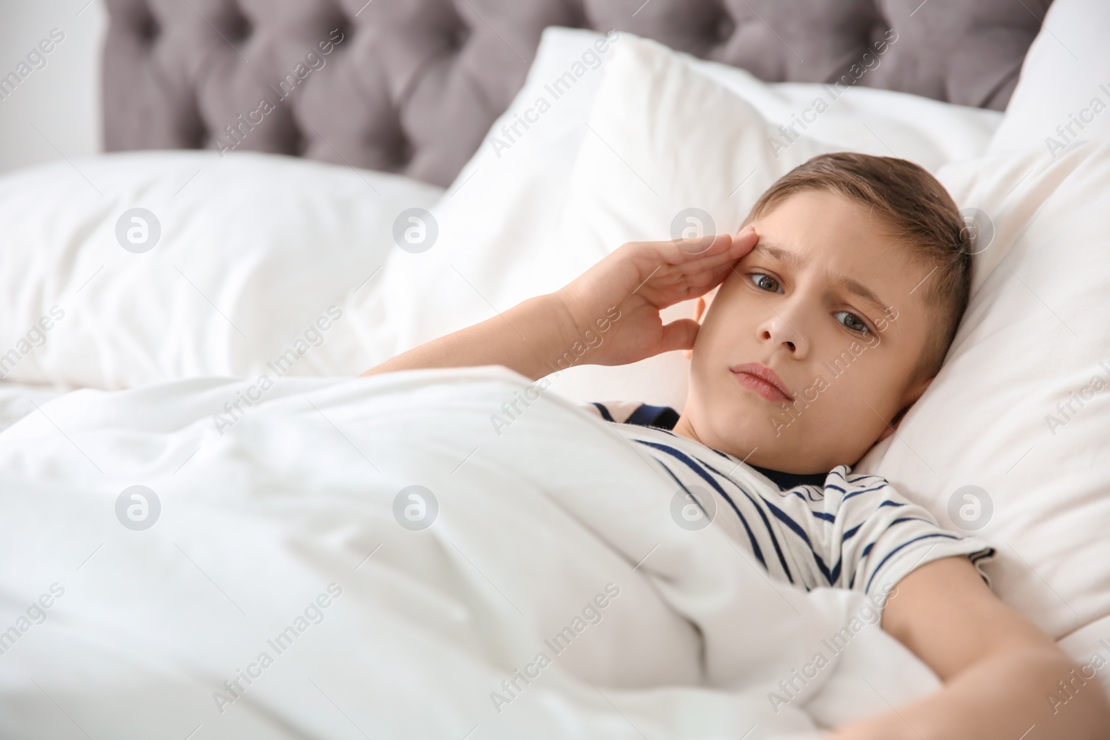 Photo of Little boy suffering from headache while lying in bed at home