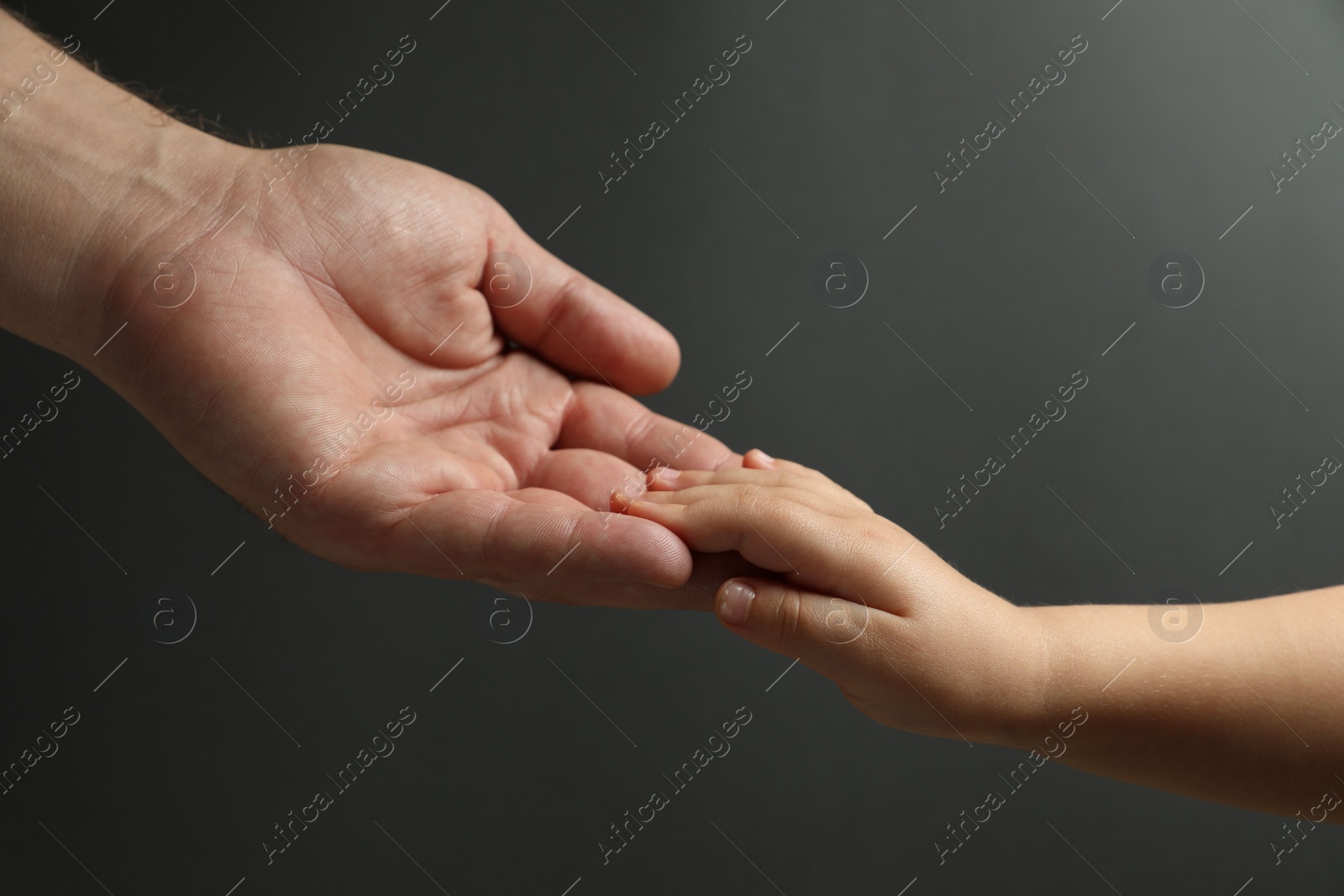 Photo of Father and child holding hands on dark grey background, closeup