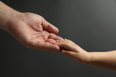 Photo of Father and child holding hands on dark grey background, closeup