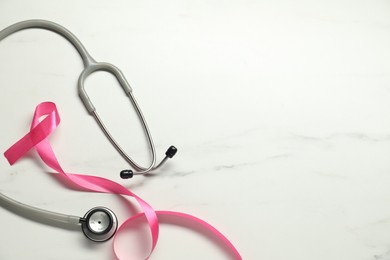 Photo of Breast cancer awareness. Pink ribbon and stethoscope on white marble table, flat lay. Space for text