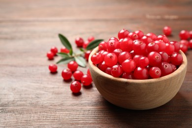 Photo of Tasty ripe cranberries on brown wooden table, closeup. Space for text