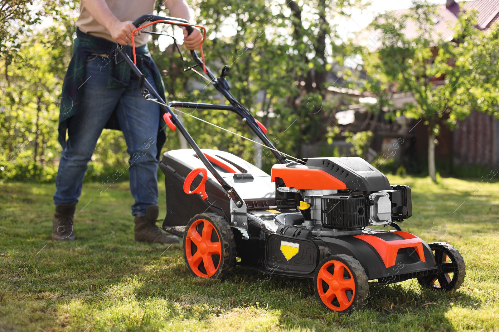 Photo of Man cutting green grass with lawn mower in garden, selective focus