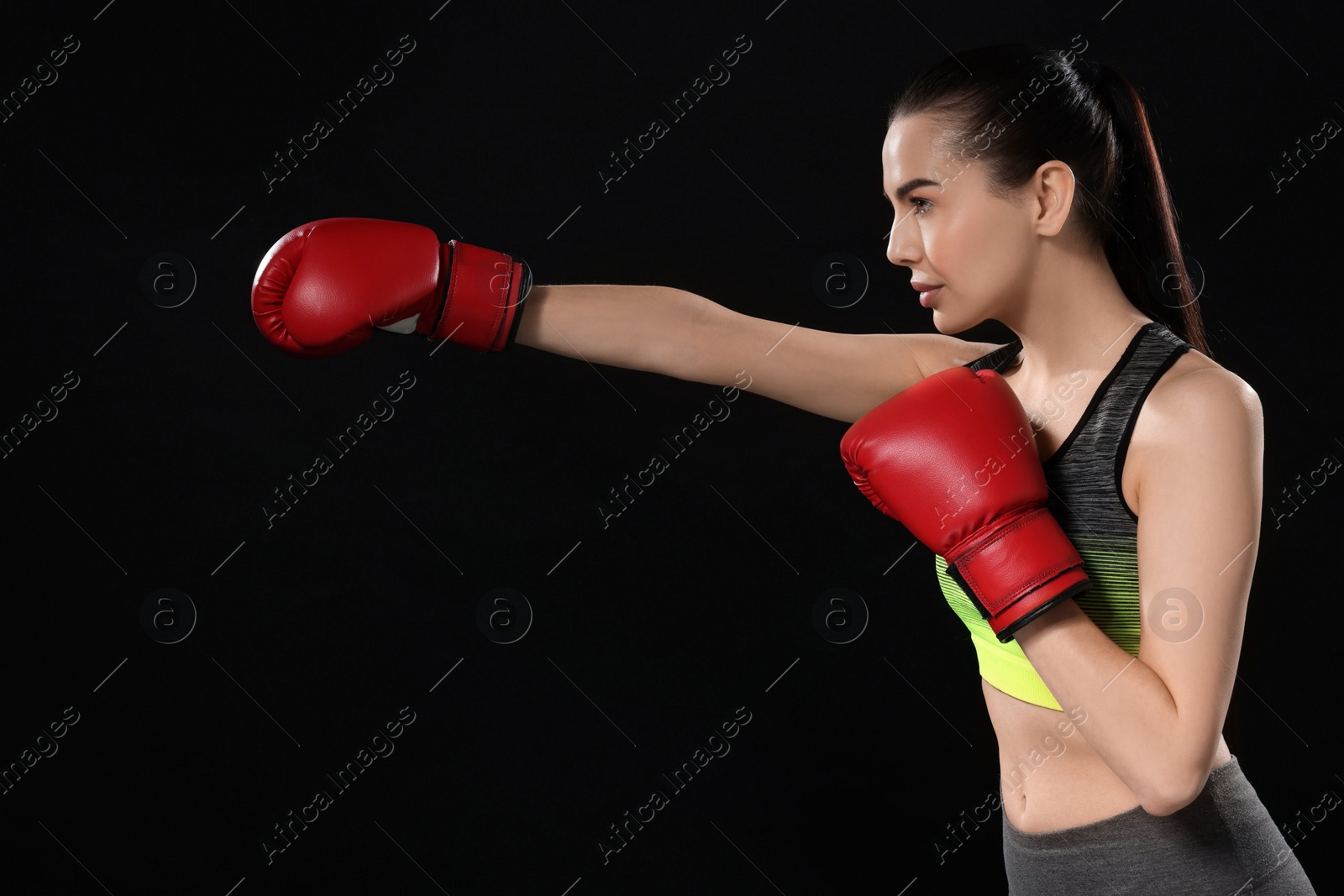 Photo of Beautiful woman in boxing gloves training on black background. Space for text