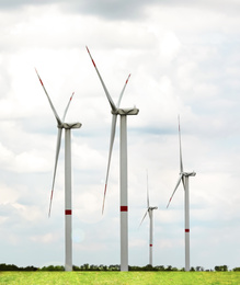 Image of Alternative energy source. Wind turbines in field under cloudy sky