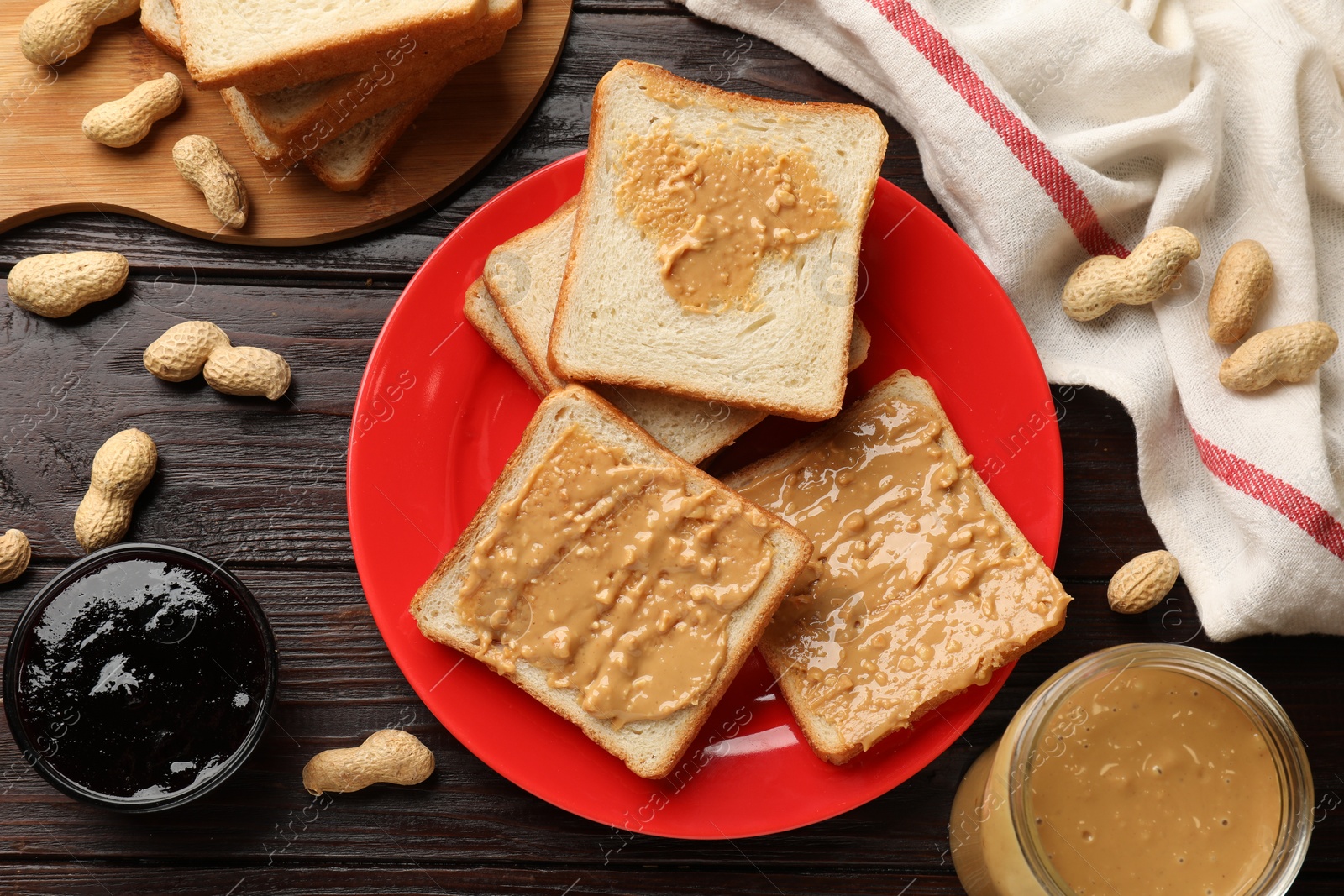 Photo of Delicious toasts with peanut butter, nuts and jam on dark wooden table, flat lay