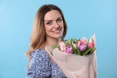 Happy young woman with bouquet of beautiful tulips on light blue background