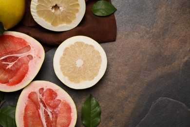 Photo of Fresh cut pomelo fruits with green leaves on dark table, flat lay. Space for text