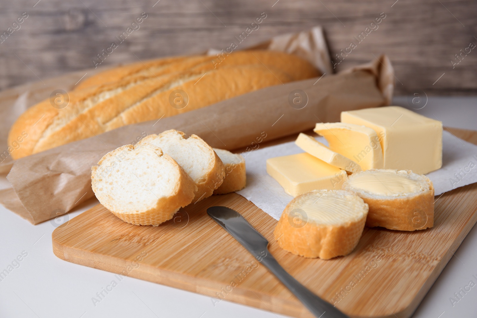 Photo of Tasty cut baguette with fresh butter on white table