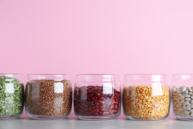 Glass jars with different types of groats on grey marble table