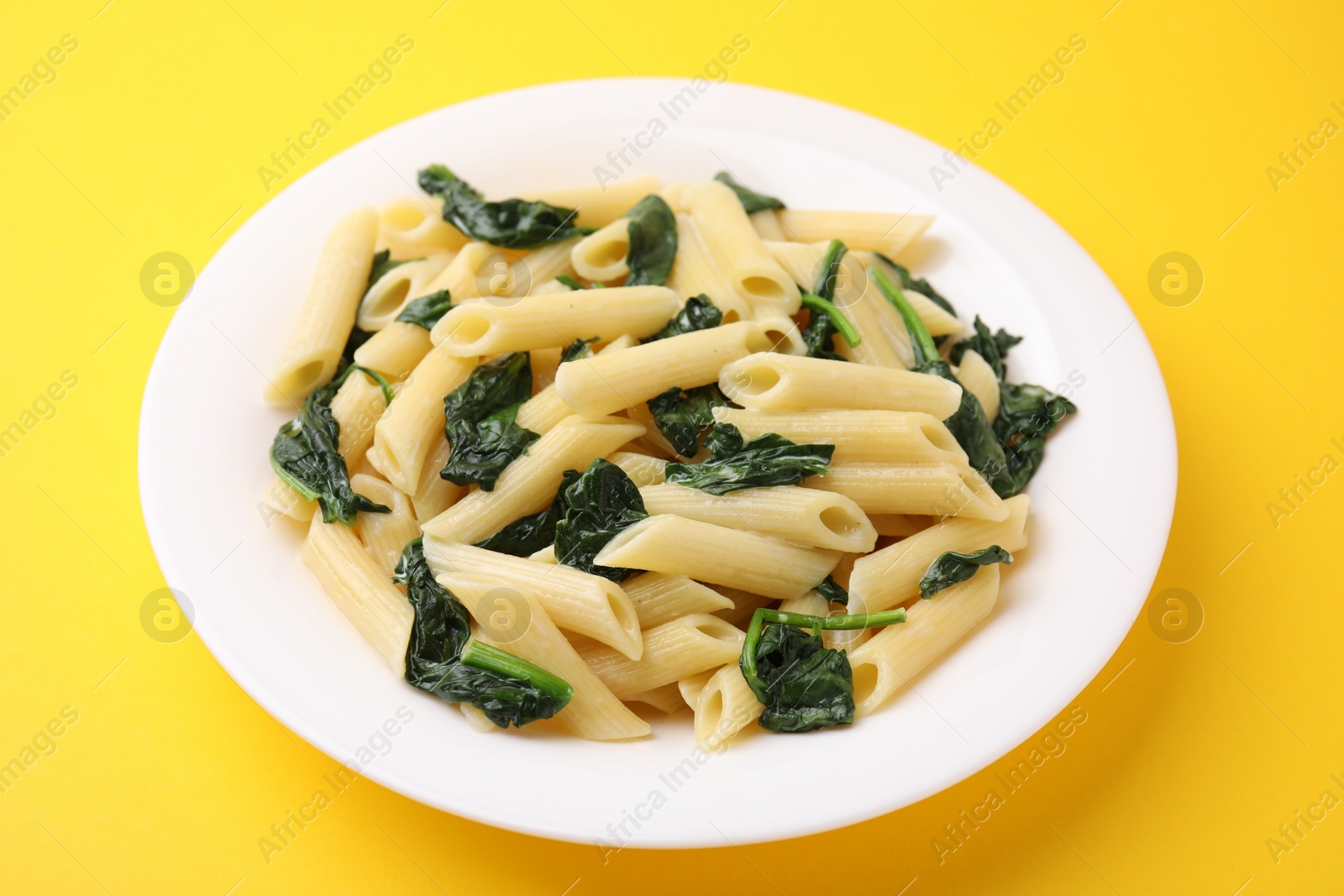 Photo of Tasty pasta with spinach and sauce on yellow table