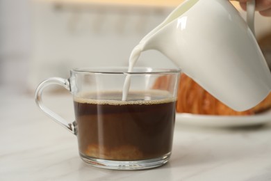 Photo of Pouring milk in coffee at white table, closeup