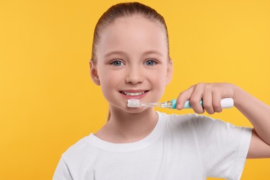 Happy girl brushing her teeth with electric toothbrush on yellow background