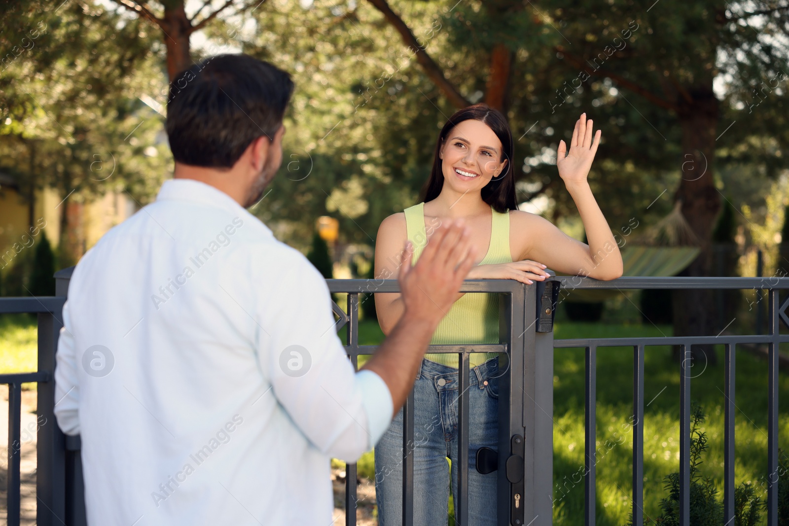 Photo of Friendly relationship with neighbours. Happy woman greeting man near fence outdoors