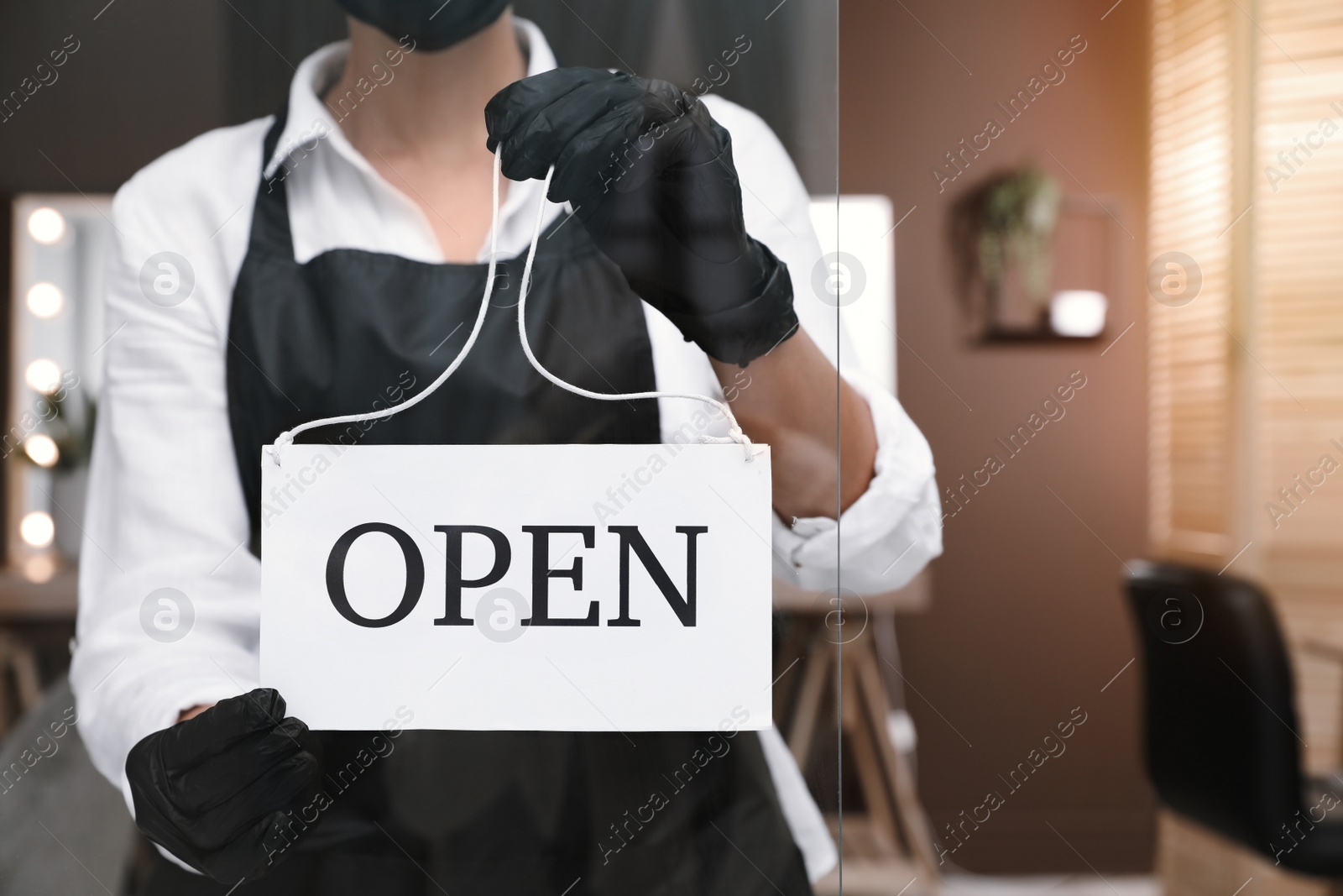 Photo of Woman hanging Open sign onto glass door in salon, closeup. Beauty services during Coronavirus quarantine