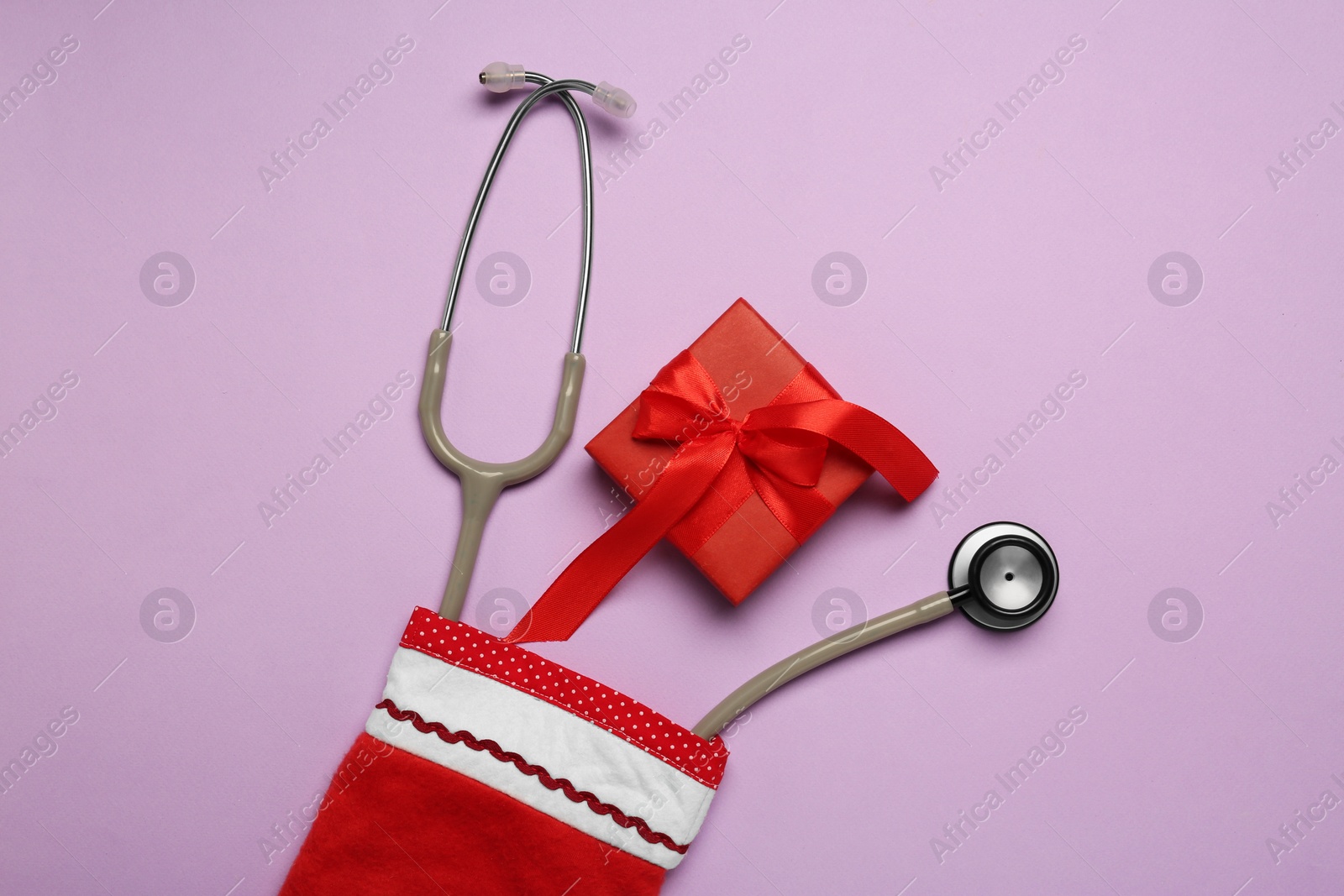 Photo of Greeting card for doctor with stethoscope and Christmas gift on purple background, flat lay