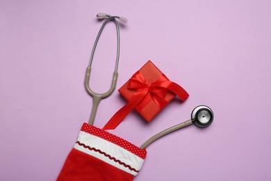 Greeting card for doctor with stethoscope and Christmas gift on purple background, flat lay