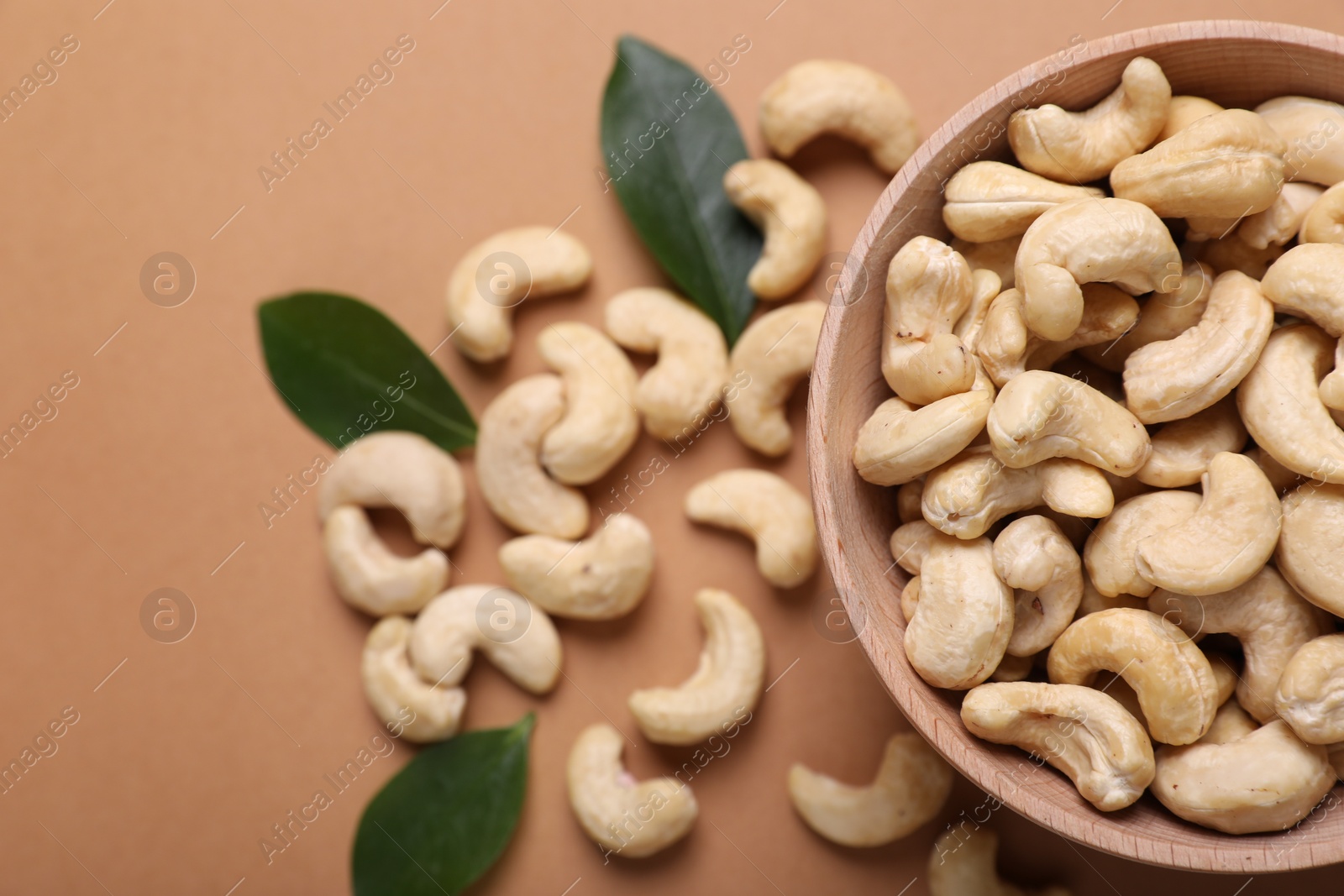 Photo of Tasty cashew nuts and green leaves on pale brown background, top view